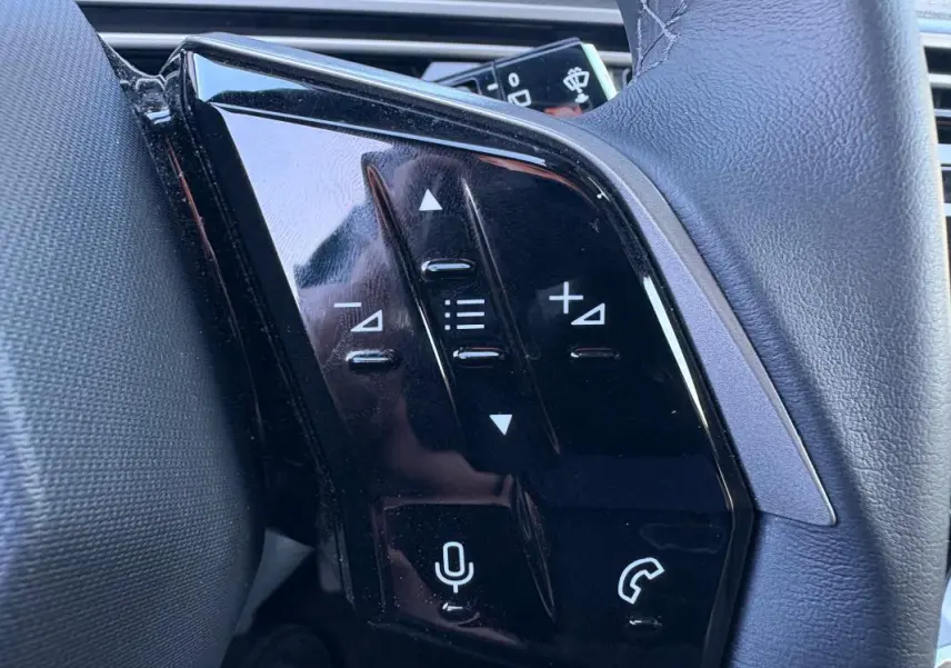 Gros plan sur les commandes tactiles noires à gauche du volant du Peugeot 5008 bleu foncé Hybrid 2025.