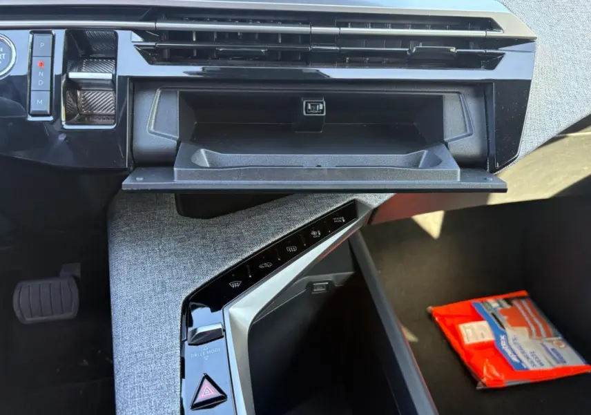 Vue intérieure du tableau de bord côté passager du Peugeot 5008 bleu foncé 2025, avec boîte automatique et rangement ouvert.