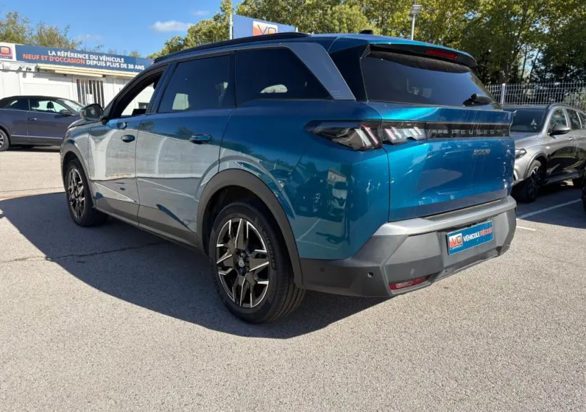 Vue 3/4 arrière droite d’un Peugeot 5008 Hybrid bleu foncé 2025 avec feux arrière distinctifs et jantes noires stylisées.