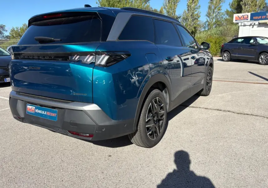 Vue 3/4 arrière droite d’un Peugeot 5008 Hybrid bleu foncé 2025 avec feux arrière distinctifs et jantes noires.