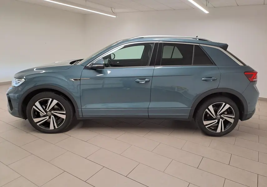 Volkswagen T-Roc 1.5 TSI R-Line bleu pétrole vu de profil côté gauche en intérieur, jantes alliage distinctives.