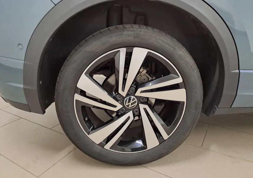 Gros plan sur la roue avant droite du Volkswagen T-Roc bleu pétrole, mettant en valeur la jante alliage bicolore au design moderne.