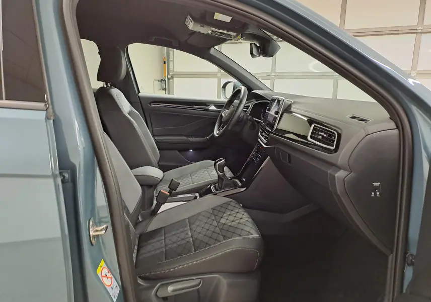 Vue intérieure côté conducteur du Volkswagen T-Roc bleu pétrole 2025, sièges avant en tissu avec surpiqûres et tableau de bord moderne.