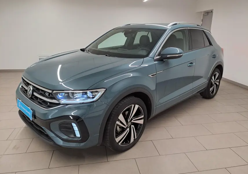 Volkswagen T-Roc 1.5 TSI R-Line bleu pétrole en 3/4 avant droit, phares allumés et jantes distinctives.