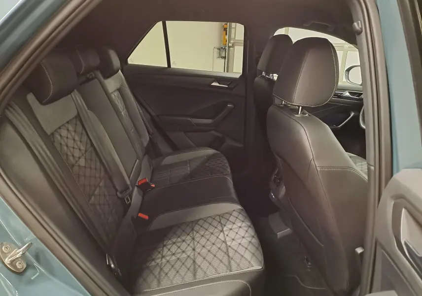 Vue intérieure arrière côté gauche du Volkswagen T-Roc 2025 bleu pétrole, montrant les sièges arrière en tissu et cuir avec surpiqûres.