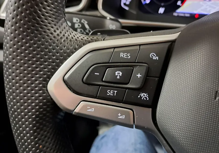 Gros plan sur les commandes au volant perforé du Volkswagen T-Roc 2025, mettant en avant les boutons de régulateur de vitesse.