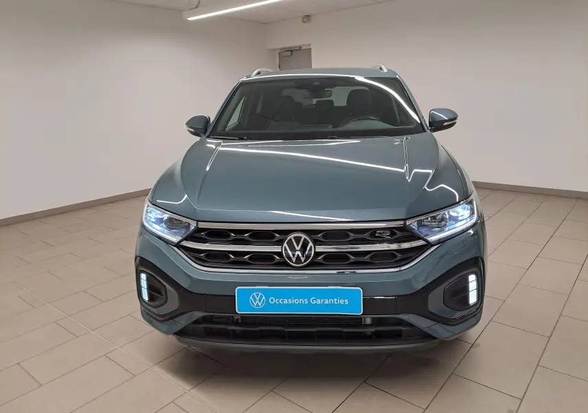 Vue avant d'un Volkswagen T-Roc 1.5 TSI 150 DSG7 R-Line bleu pétrole avec phares et feux diurnes allumés en intérieur.