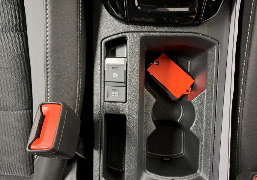 Gros plan sur la console centrale du Volkswagen T-Roc 2025, montrant frein à main électronique et porte-gobelets avec clé à étiquette rouge.