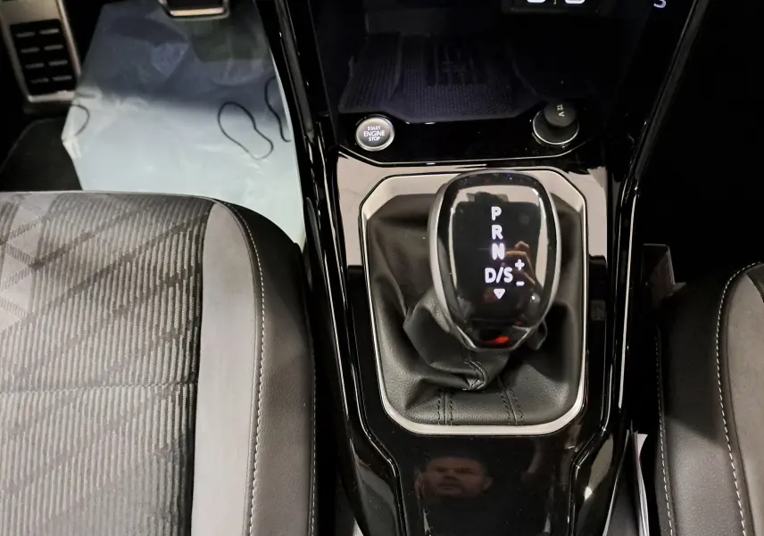 Vue rapprochée de la console centrale du Volkswagen T-Roc 1.5 TSI 150 DSG7, avec levier de vitesses automatique et sièges tissu noir.