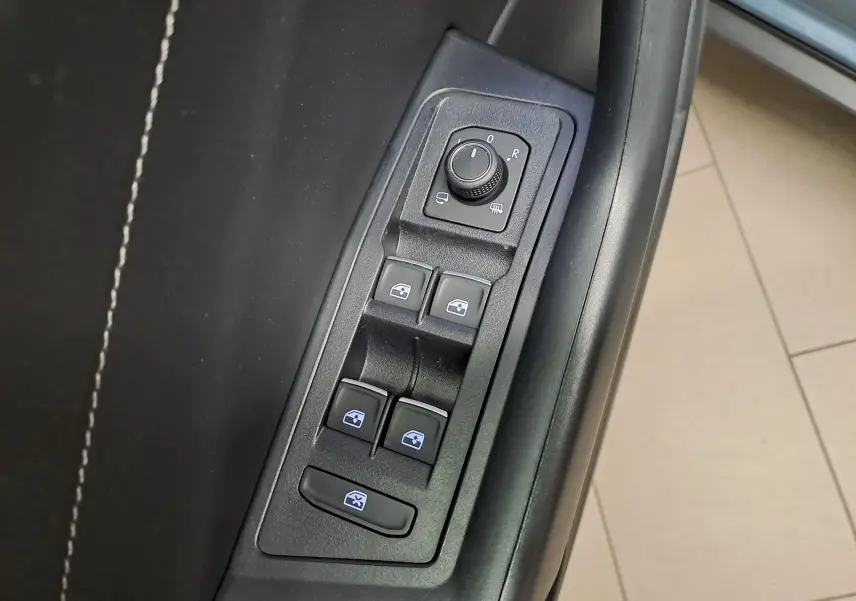 Gros plan sur les commandes de lève-vitres et réglage des rétroviseurs côté conducteur du Volkswagen T-Roc 1.5 TSI bleu pétrole 2025.
