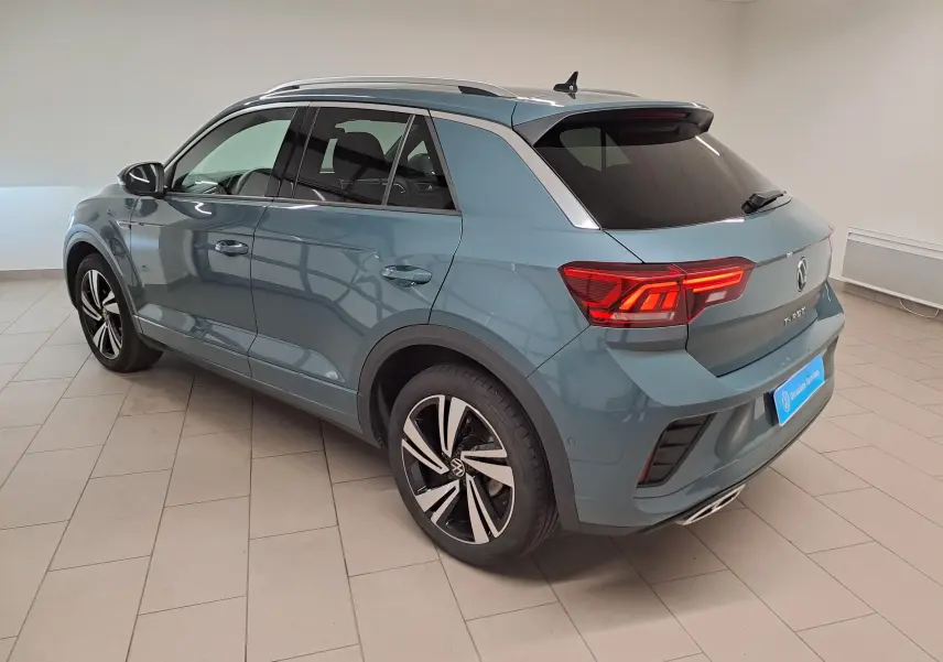 Volkswagen T-Roc 2025 bleu pétrole en vue 3/4 arrière droit, avec jantes alliage et feux arrière allumés.