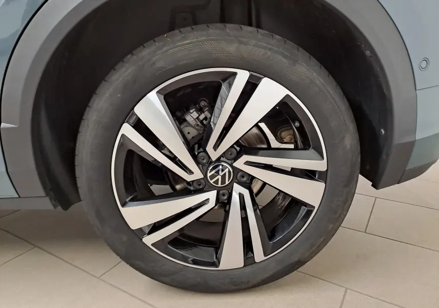 Gros plan sur la roue avant droite du Volkswagen T-Roc bleu pétrole 2025 avec jante alliage bicolore au design moderne.