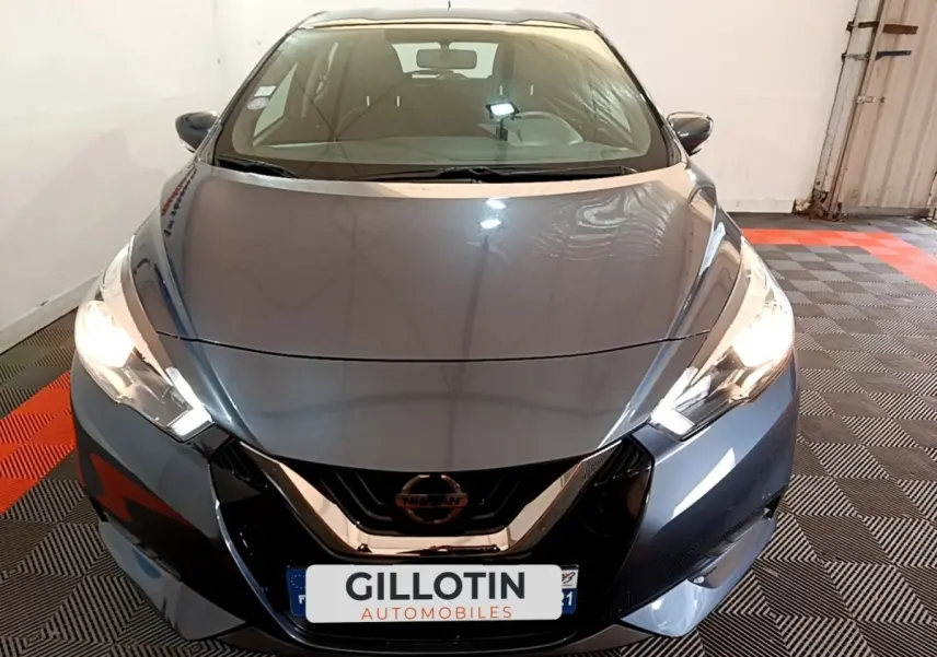 Vue avant d'une Nissan Micra IG-T 100 Business Edition gris foncé avec phares allumés dans un garage.