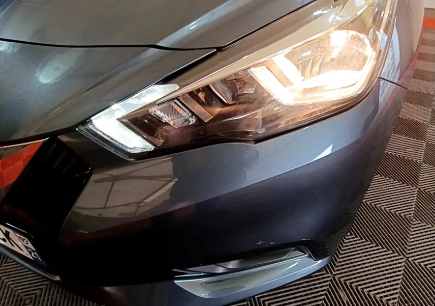 Gros plan sur l'avant droit gris foncé d'une Nissan Micra 2020 avec phare allumé et clignotant LED visible.
