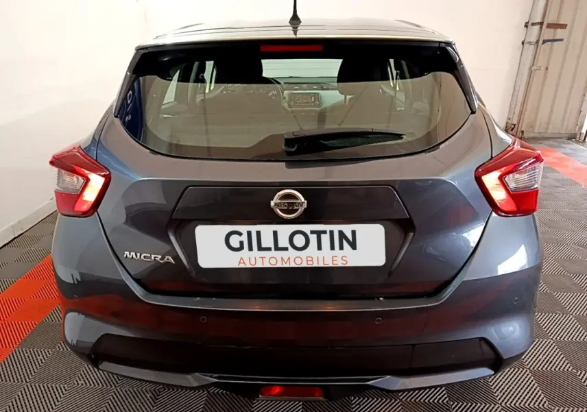 Vue arrière d'une Nissan Micra gris foncé avec feux arrière LED et logo Nissan visible sur un sol à damiers noir et rouge.