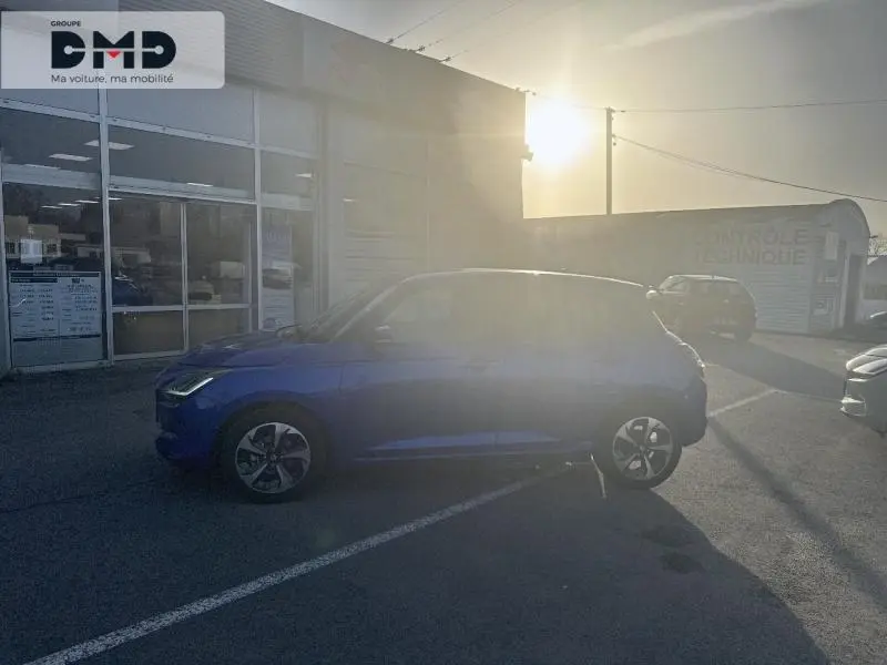 Vue de profil côté gauche d'une Suzuki Swift 1.2 Hybrid 83ch Pack en bleu Frontier Pearl Metal stationnée en extérieur au soleil couchant.