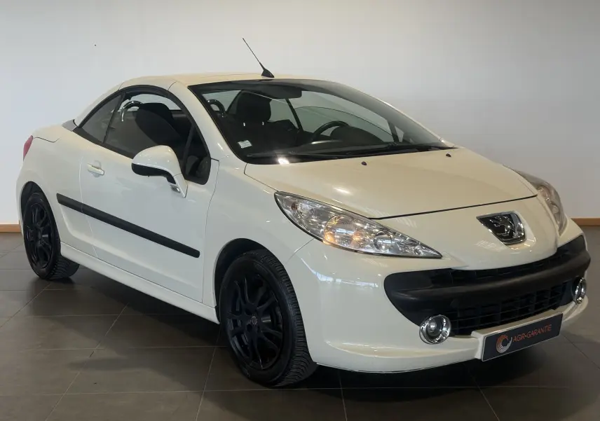 Peugeot 207 CC beige vue 3/4 avant droit, cabriolet fermé, jantes noires et phares allumés.