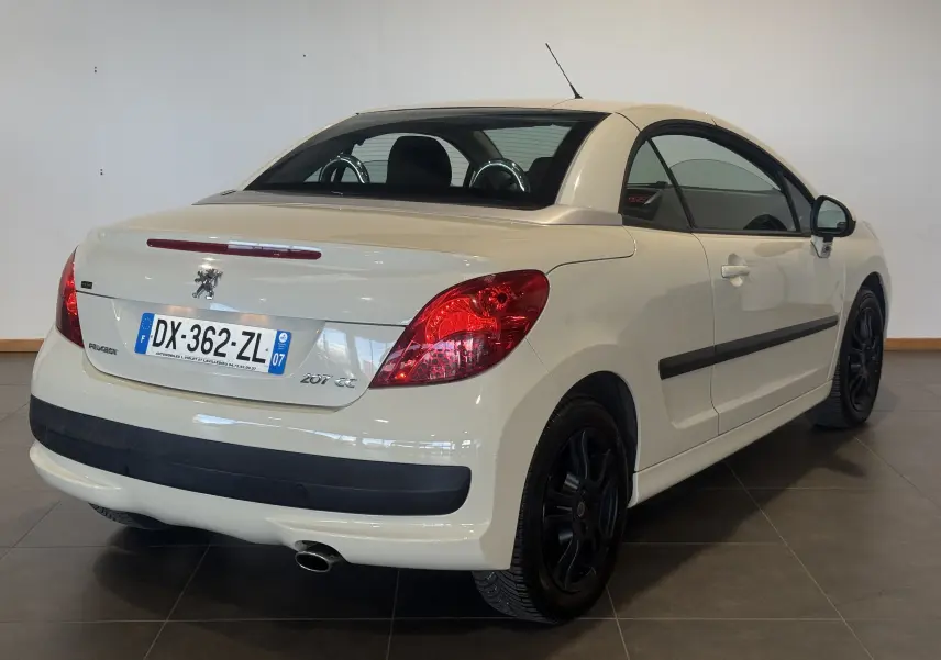 Vue 3/4 arrière droite d'un cabriolet Peugeot 207 CC beige de 2007 avec jantes noires et toit rigide fermé.