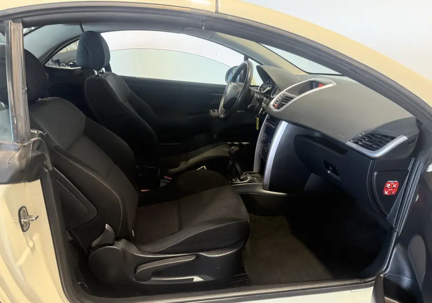 Vue intérieure côté conducteur du cabriolet Peugeot 207 CC beige de 2007, montrant sièges noirs et tableau de bord.