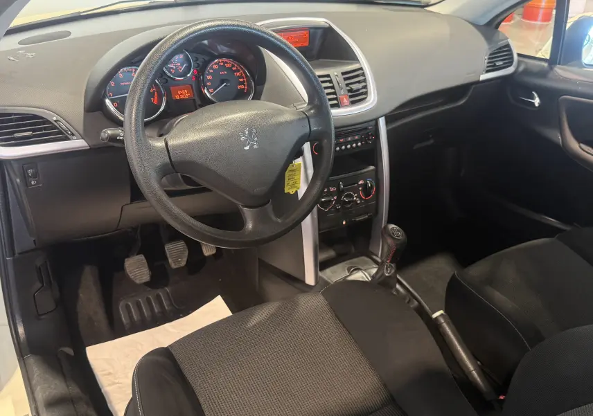 Vue intérieure côté conducteur du Peugeot 207 CC beige de 2007, montrant le volant, tableau de bord et levier de vitesse manuel.