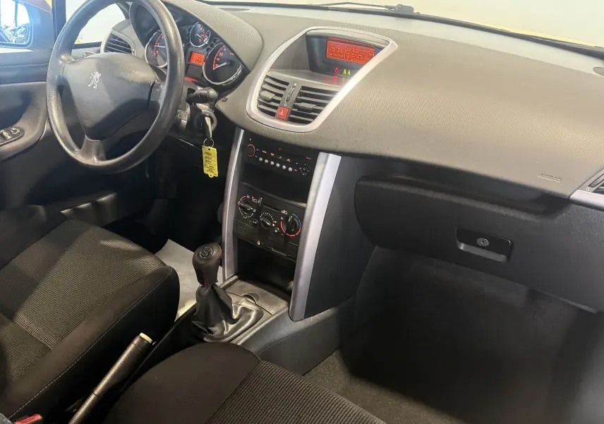 Vue intérieure côté conducteur du tableau de bord et console centrale d'une Peugeot 207 CC beige avec boîte manuelle et climatisation.