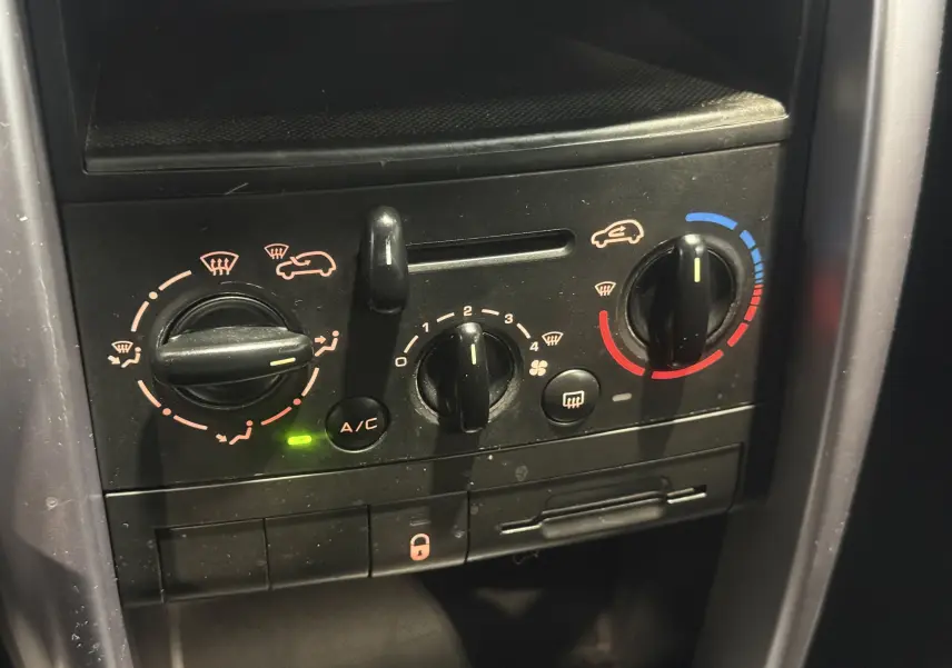 Gros plan sur les commandes de climatisation du tableau de bord du Peugeot 207 CC beige, version 2007, avec réglages manuels.