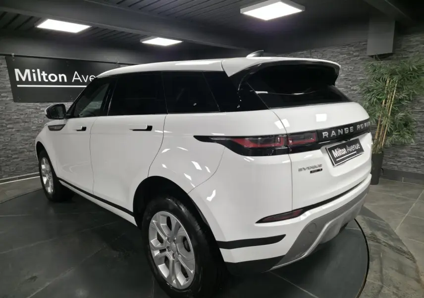 Vue 3/4 arrière droite d'un Range Rover Evoque blanc avec toit noir et jantes argentées en showroom.