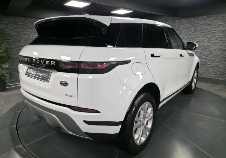 Vue 3/4 arrière droit d'un Range Rover Evoque blanc avec toit noir et jantes 18 pouces dans un showroom.
