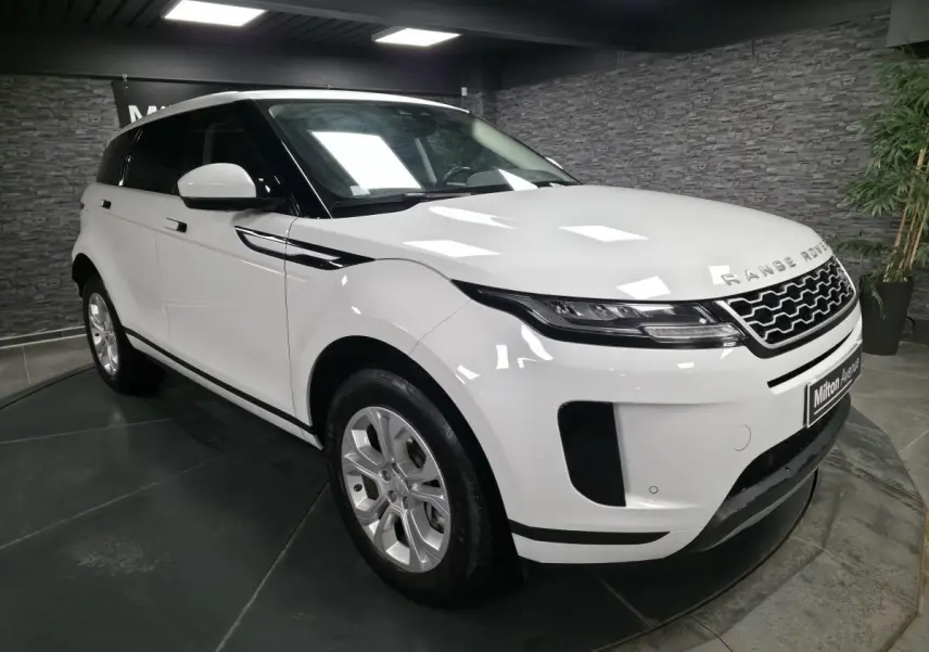 Vue 3/4 avant droite d'un Range Rover Evoque blanc avec calandre noire et jantes argentées en intérieur showroom.