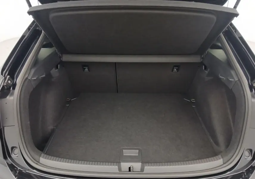 Coffre ouvert vu de l'arrière d'un Volkswagen Taigo noir intense nacré, espace de chargement vide et tapis noir.