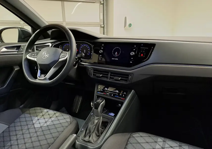 Vue intérieure avant gauche du Volkswagen Taigo 1.5 TSI R-Line 2025, avec volant cuir multifonctions et tableau de bord digital.