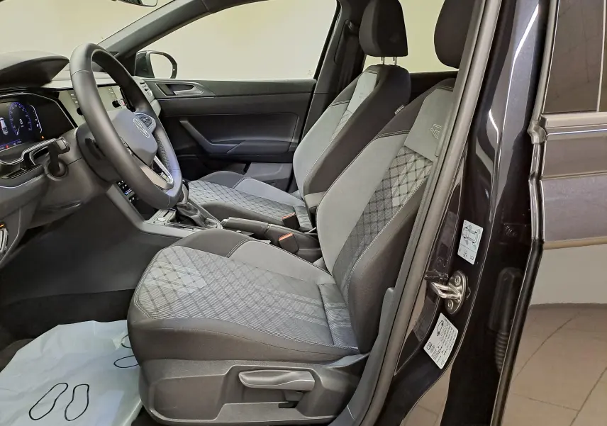 Vue intérieure côté conducteur du Volkswagen Taigo noir intense nacré, sièges avant gris à motifs et volant multifonctions cuir.