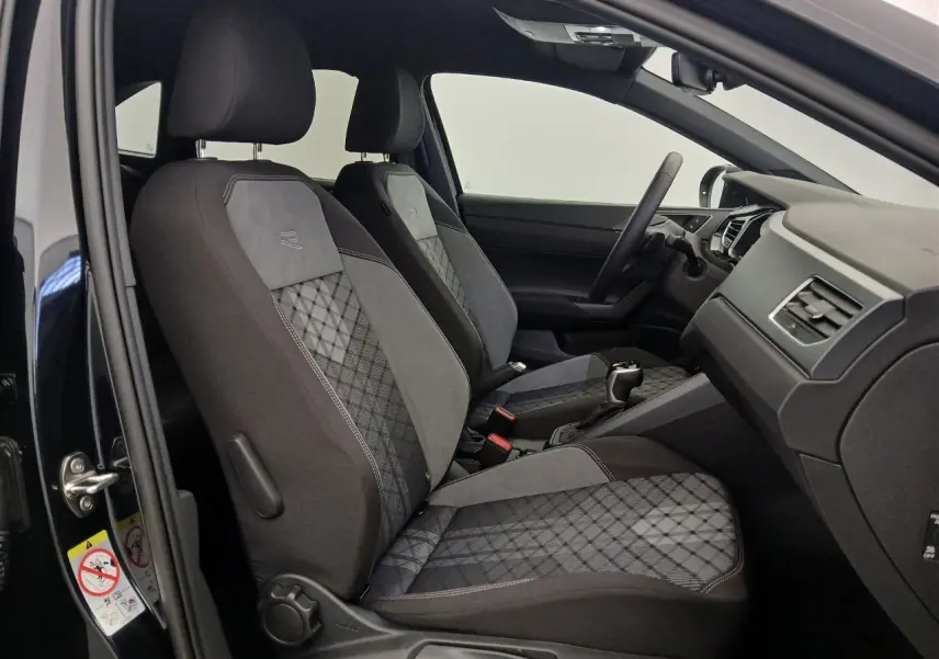 Vue intérieure côté gauche du Volkswagen Taigo 1.5 TSI R-Line 2025, sièges sport noirs avec surpiqûres grises et volant multifonctions.