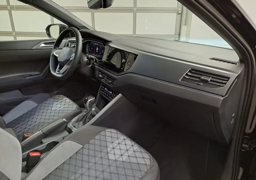 Intérieur du Volkswagen Taigo 1.5 TSI R-Line 2025, vue côté conducteur, sièges tissu gris à motifs et tableau de bord noir.