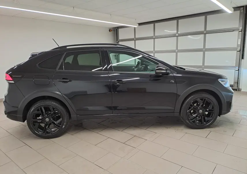 Profil droit d'un Volkswagen Taigo 2025 noir intense nacré avec jantes alliage noires 18 pouces en intérieur showroom.