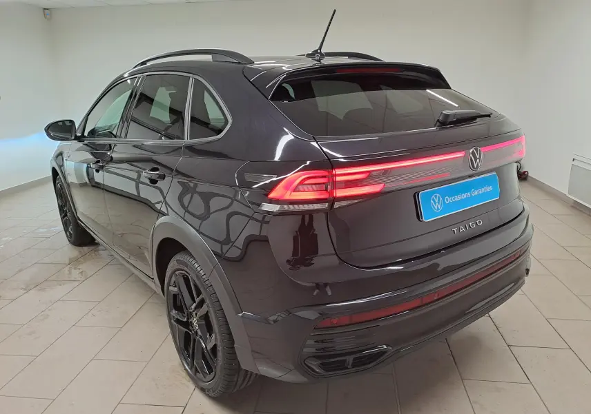 Vue 3/4 arrière droite du Volkswagen Taigo noir intense nacré avec jantes noires et feux arrière LED allumés.