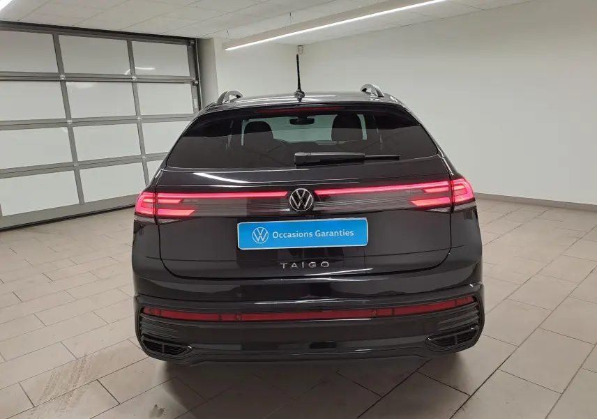 Vue arrière d'un Volkswagen Taigo noir intense nacré avec feux arrière allumés et logo VW visible.