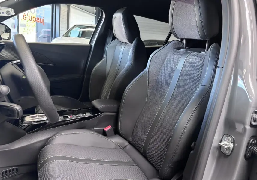 Vue intérieure côté conducteur du Peugeot 2008 gris selenium, mettant en valeur les sièges bi-matière avec surpiqûres vertes et volant compact cuir.