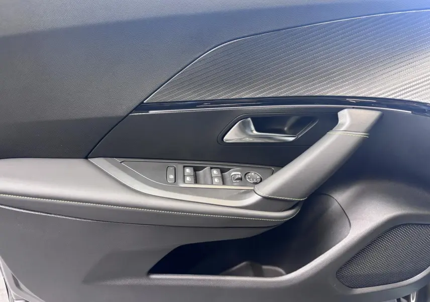 Détail de la porte avant gauche du Peugeot 2008 gris selenium, avec commandes de vitres et insert carbone.