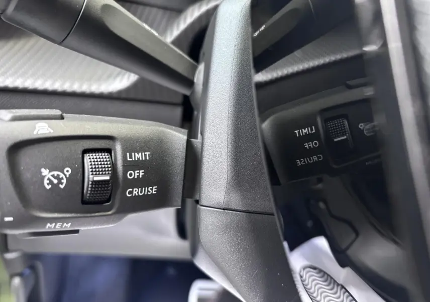 Gros plan sur la commande de régulateur de vitesse noire du Peugeot 2008 1.2i Hybrid, intérieur gris selenium.