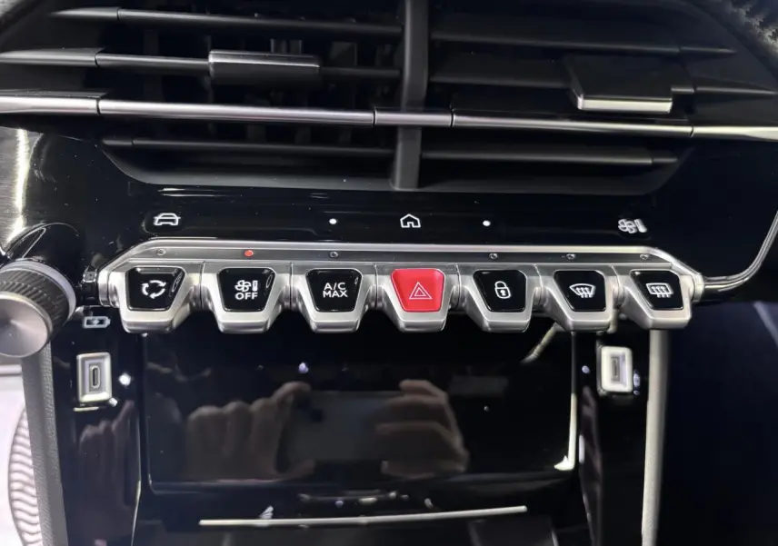 Gros plan sur la console centrale noire brillante du Peugeot 2008 1.2i Hybrid avec boutons argentés et rouge d'alerte.