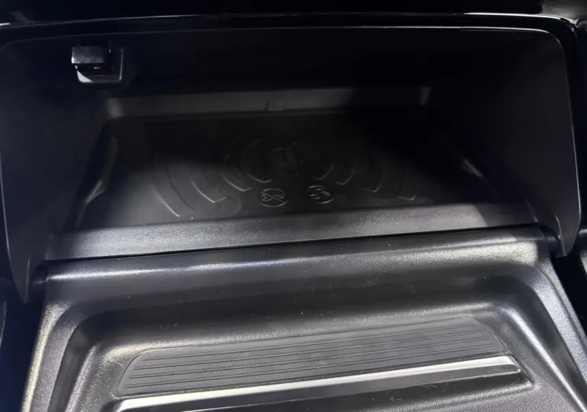 Gros plan sur le compartiment de rangement avant avec chargeur sans fil dans le Peugeot 2008 gris selenium.