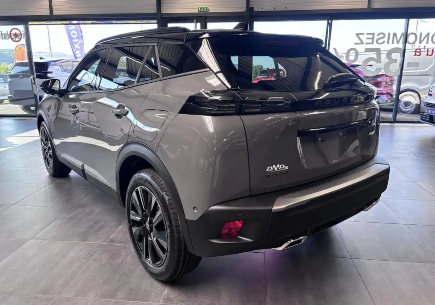 Vue 3/4 arrière droite du Peugeot 2008 gris selenium avec toit noir et jantes alliage bi-ton dans un showroom.