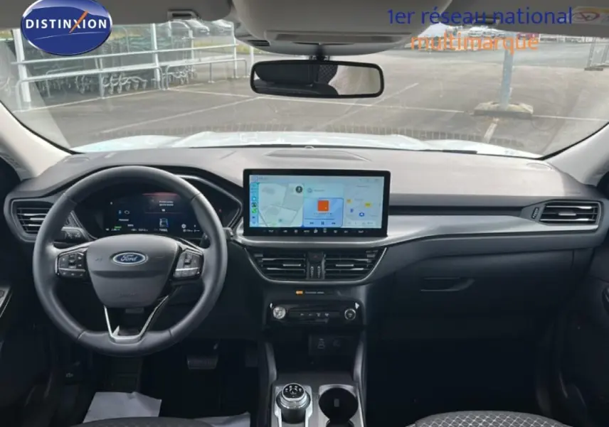 Vue intérieure frontale du tableau de bord noir du Ford Kuga blanc 2025 avec écran tactile central et volant multifonction.