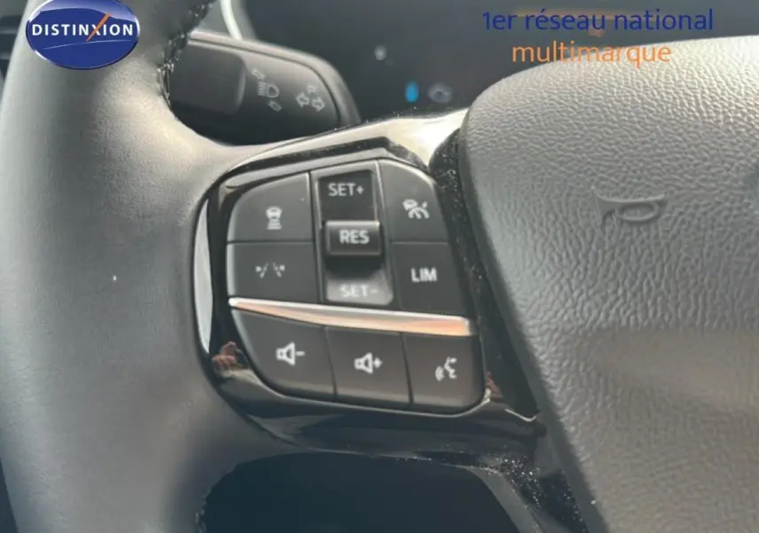 Gros plan sur les commandes au volant côté gauche du Ford Kuga blanc 2025 avec régulateur et limiteur de vitesse.