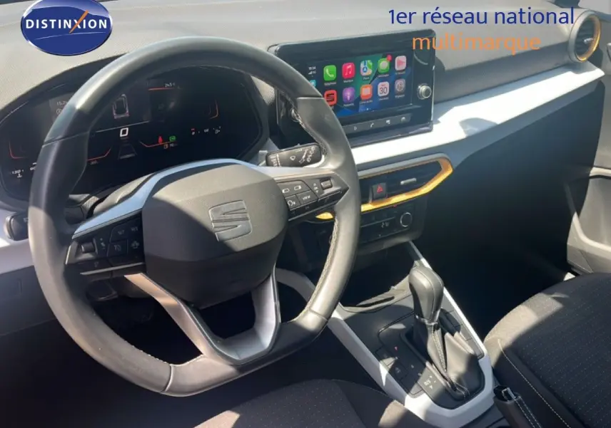Vue intérieure centrée sur le volant et la console centrale du SEAT Arona 2025, avec écran tactile et détails noirs et blancs.