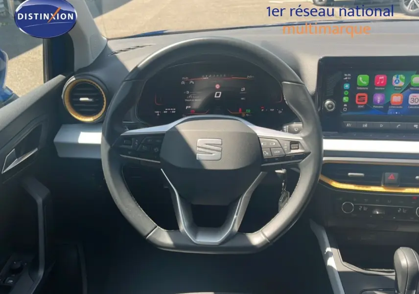Vue intérieure centrée sur le volant noir du SEAT Arona 2025, avec tableau de bord digital et écran tactile coloré.