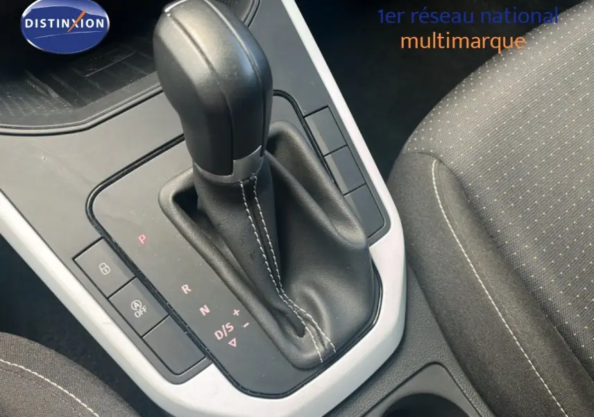 Gros plan sur la commande de boîte automatique noire dans l’habitacle d’un SEAT Arona 2025, siège tissu gris visible.