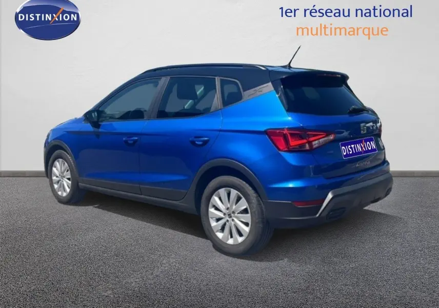 Vue 3/4 arrière droite d'un SEAT Arona bleu saphir métal avec toit noir, stationné sur sol gris.
