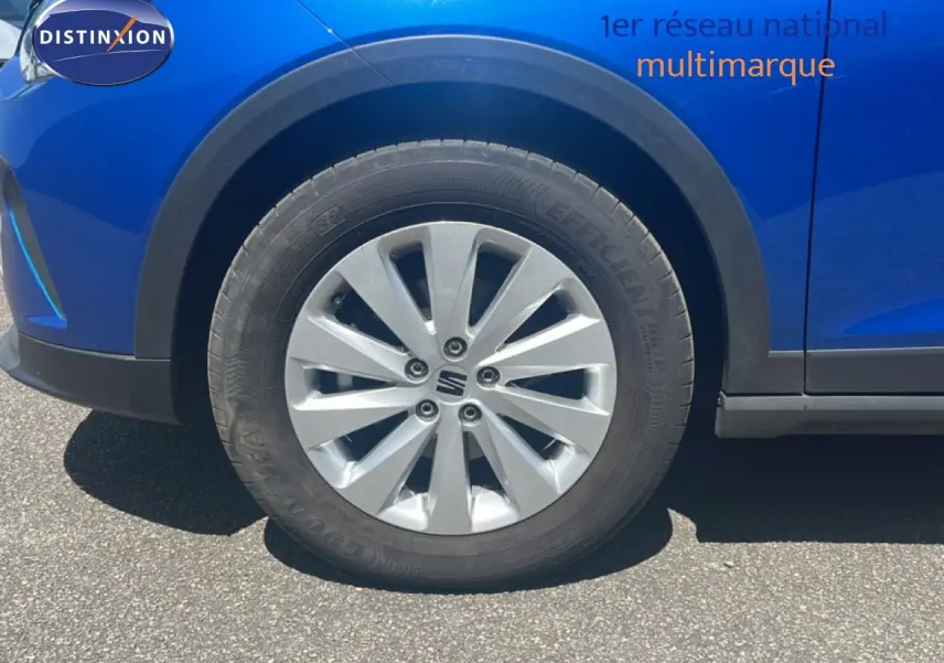 Gros plan sur la roue avant gauche d'un SEAT Arona bleu saphir métal avec jante argentée et partie de la carrosserie visible.